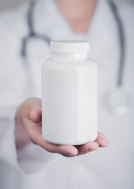 Doctor holding plastic container of pills on grey hospital wall surface. Antibiotics, vitamins and virus treatment tablet.