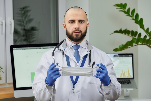 A doctor holding a protective face mask in his office.