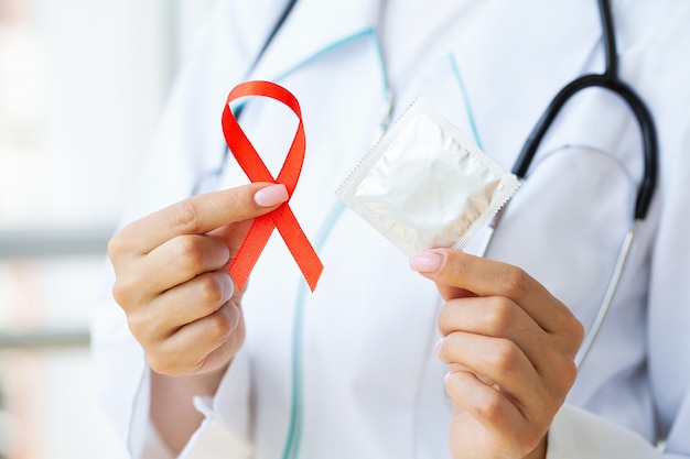 Doctor holding a red ribbon and condom calling for safe sex and protection from AIDS