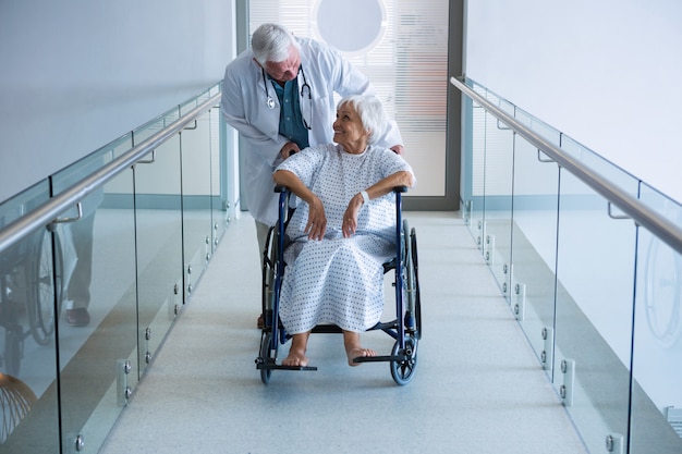 Doctor holding senior patient on wheelchair in passageway