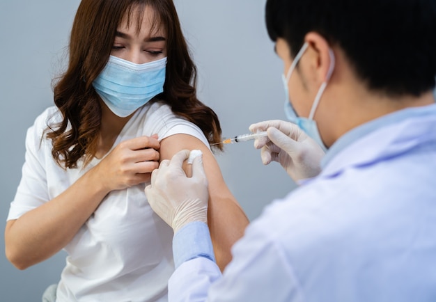 Doctor holding syringe and using cotton before make injection to patient in a medical mask. Covid-19 or coronavirus vaccine