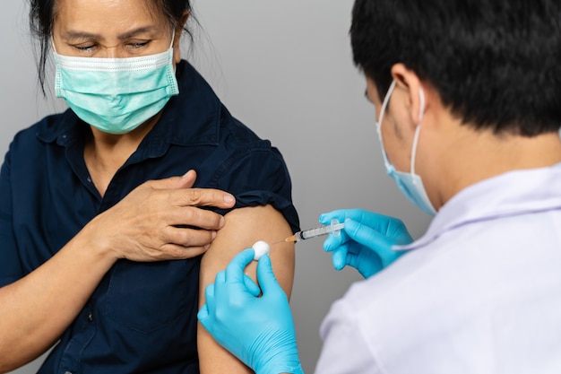 Doctor holding syringe and using cotton before make injection to woman in a medical mask. Covid-19 or coronavirus vaccine