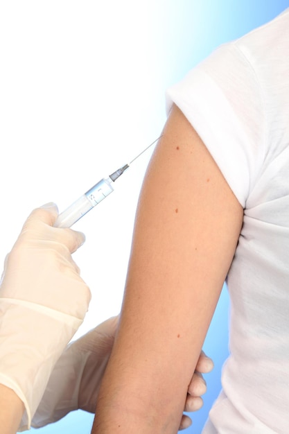 Doctor holding syringe with a vaccine in the patient shoulder on blue background