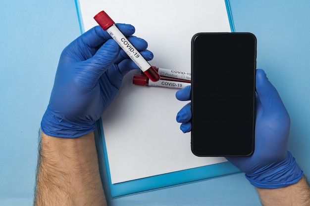 Photo doctor holding test tube with blood for 2019-ncov analyzing and smartphone.