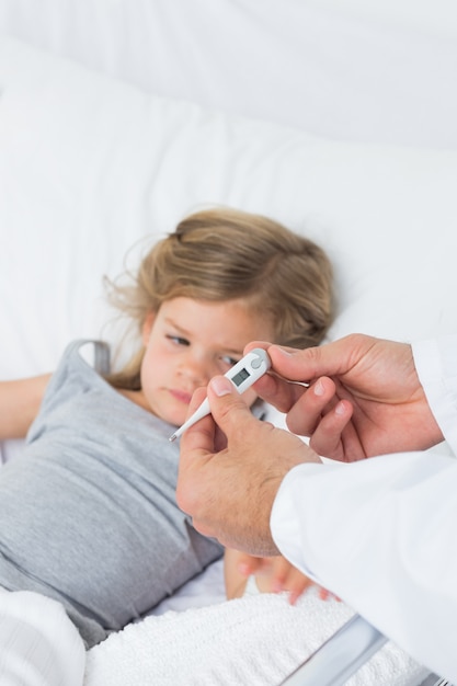 Doctor holding thermometer with ill girl in hospital