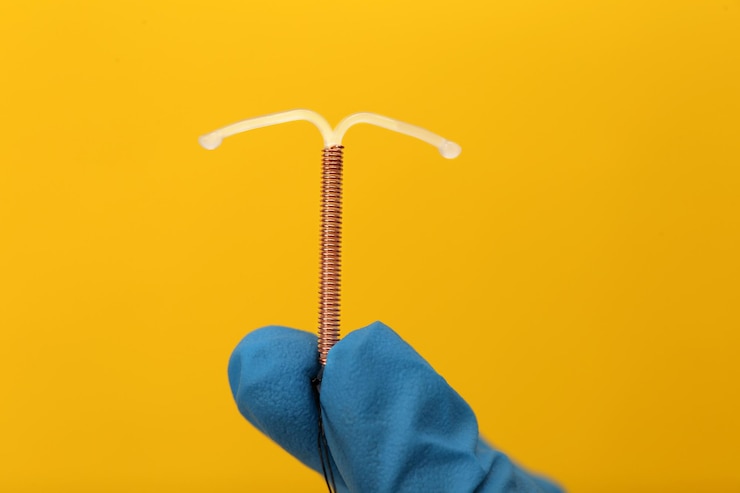 Photo doctor holding tshaped intrauterine birth control device on yellow background closeup