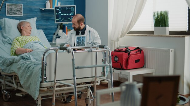 Doctor holding x ray scan on tablet for retired ill patient