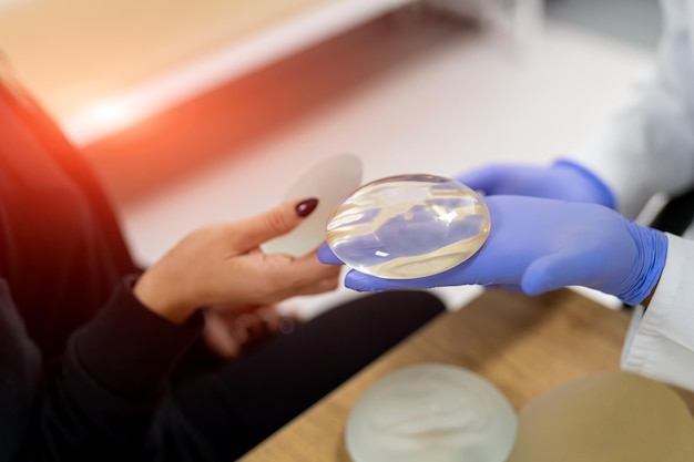 Doctor holds breast implants next to patient Visit to female breast plastic surgery clinic Consultation with an experienced surgeon Female breast implant selection