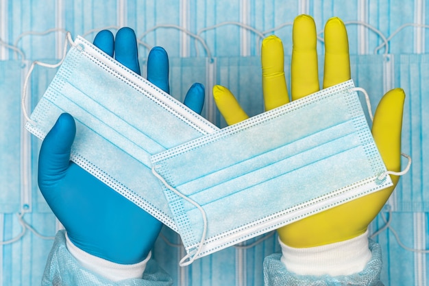 doctor holds  face mask in blue glove in one hand and other surgical face mask in yellow glove