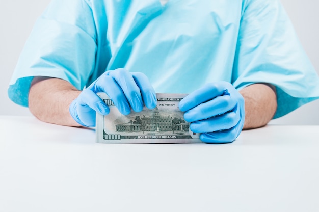 Doctor holds one hundred dollar bills. The concept of corruption in medicine