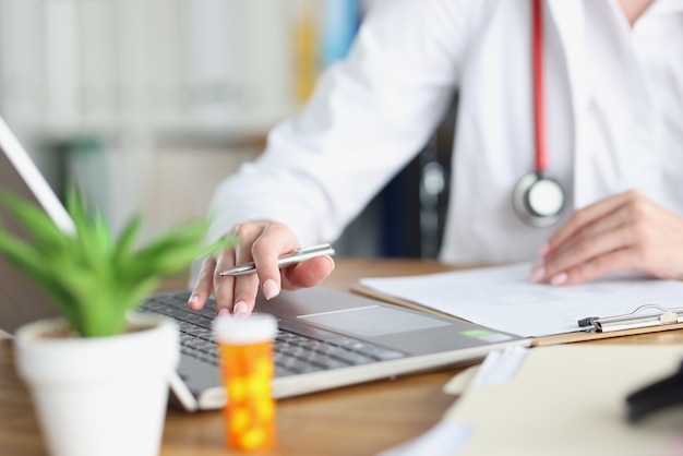 Doctor holds pen and works on laptop in medical office