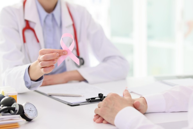 Doctor holds pink ribbon showing support for patient at appointment in clinic symbol of breast