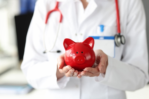 Doctor holds red pig piggy bank in his hands