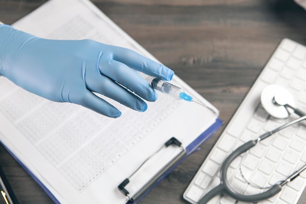 The doctor holds a syringe by the table