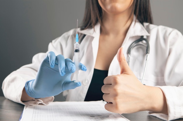 The doctor holds a syringe and shows a thumb up