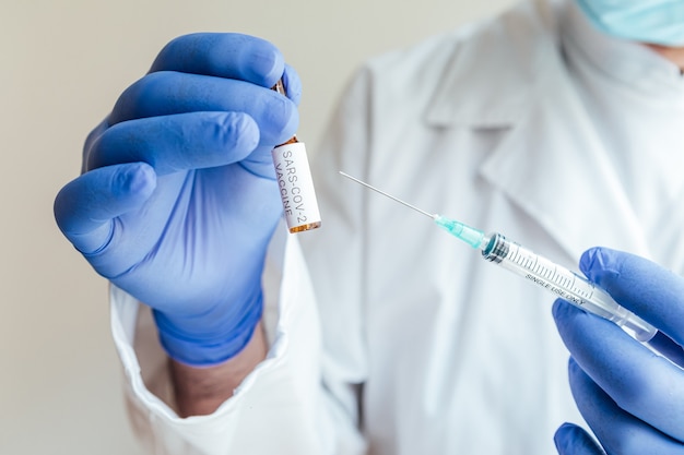 Doctor holds a syringe with a needle in one hand and a container with the COVID-19 vaccine in the other.