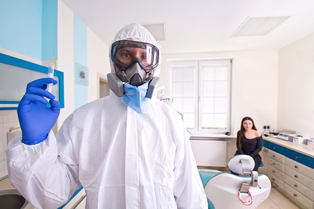 Doctor in de beschermende pak uniform en masker houdt injectiespuit met vaccin.