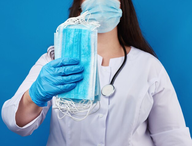 Doctor in een witte jas en masker heeft een stapel maskers