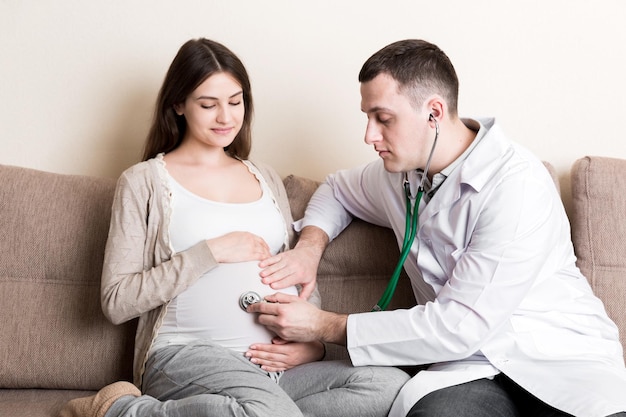 Doctor is checking pregnant woman's belly with a stethoscope Physician is listening to a heartbeat of a baby