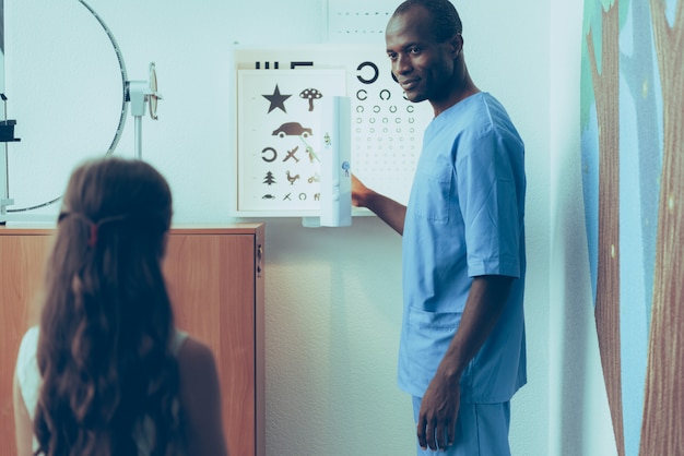 Photo doctor is examining eyes of girl on eye chart