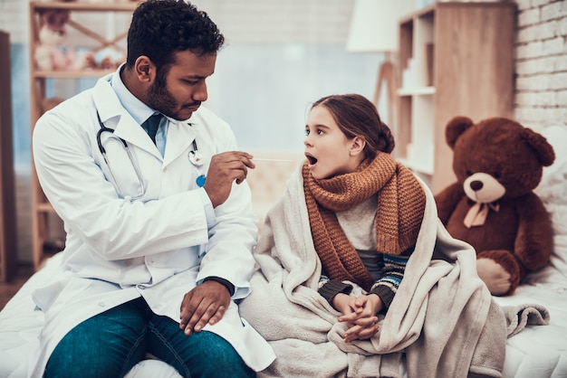 Doctor is examining throat of little girl with cold.