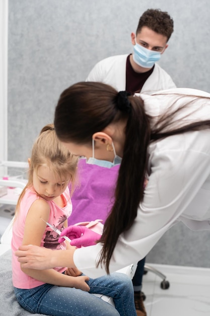 Foto il dottore sta dando un'iniezione a una ragazzina il bambino fissa in una ciotola di soffocamento vaccino preventivo per bambini piccoli vista ravvicinata il medico è in piedi sul retro