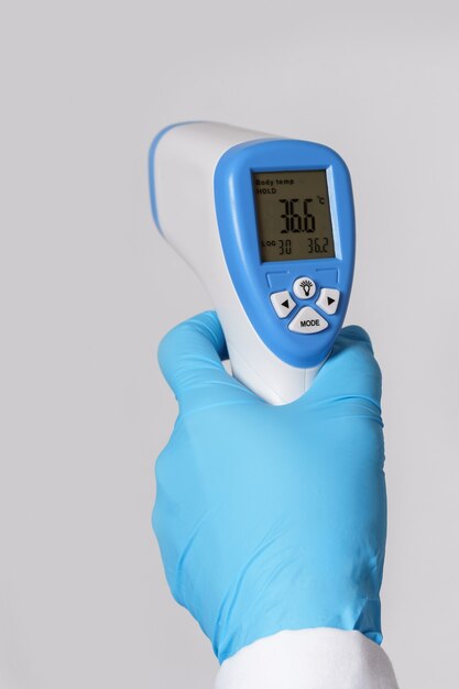 Doctor is holding a digital infrared thermometer on gray wall