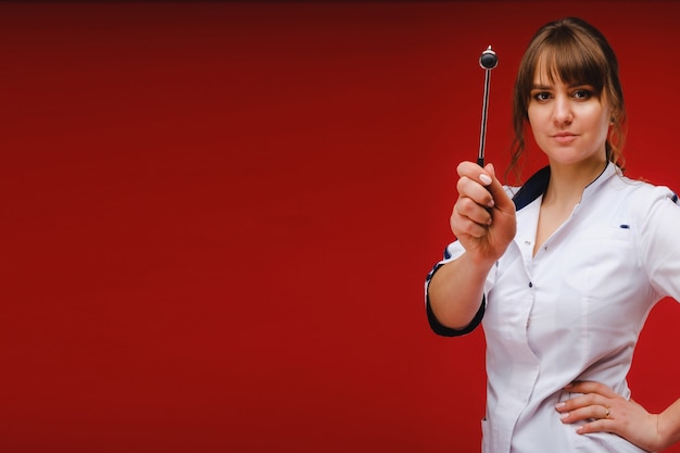 The doctor is holding a neurological hammer on a red background. The neurologist checks the patient's reflexes with a hammer. Diagnostics, healthcare, and medical care.