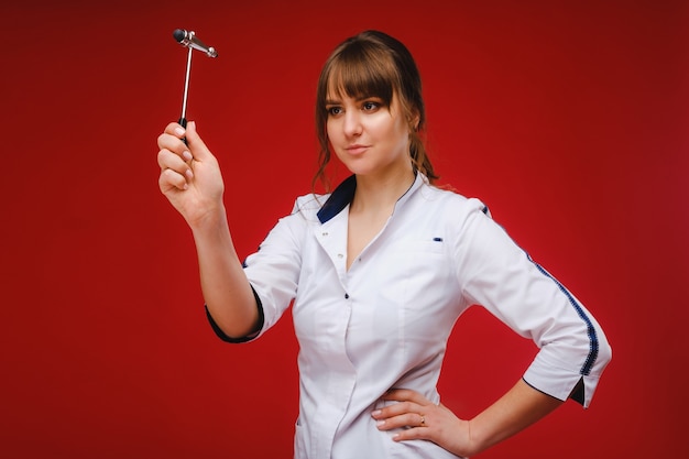 The doctor is holding a neurological hammer on a red background. The neurologist checks the patient's reflexes with a hammer. Diagnostics, healthcare, and medical care