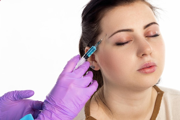 The doctor is injecting a botox into lips of the patient  against the white background