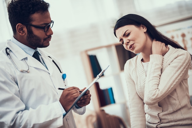 Doctor is listening to woman's symptoms. Woman's neck hurts.