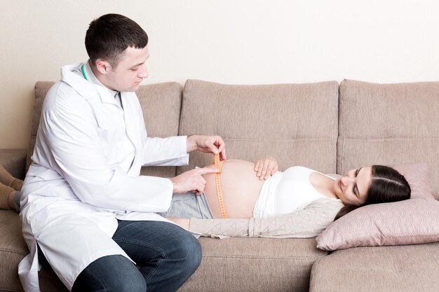 医師は自宅で妊娠中の患者の成長する腹部を測定しています 妊娠の概念