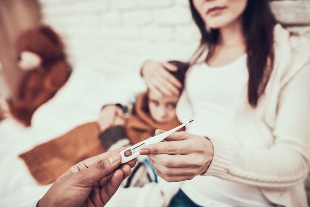 Doctor is taking temperature of pregnant mother and daughter