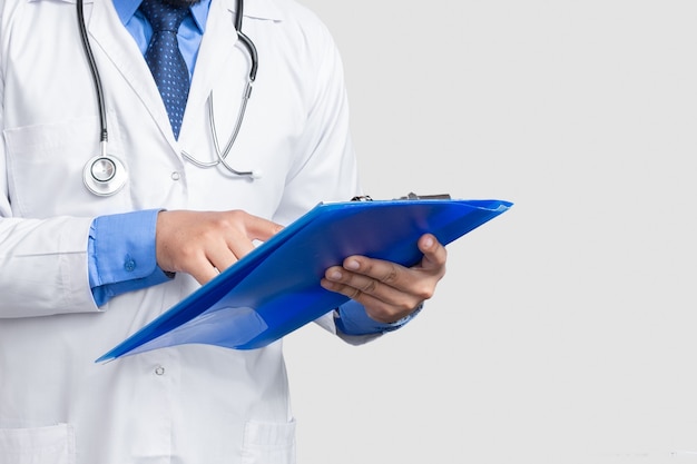 Doctor in lab coat holding and reading patient file or medical notes looking, isolated on white wall