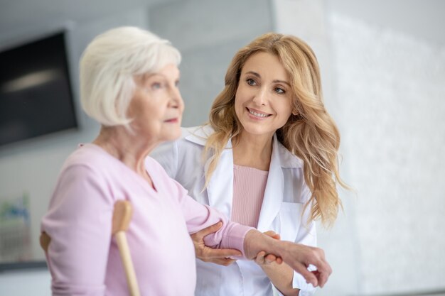 Doctor in a lab coat supporting her patient and looking at her