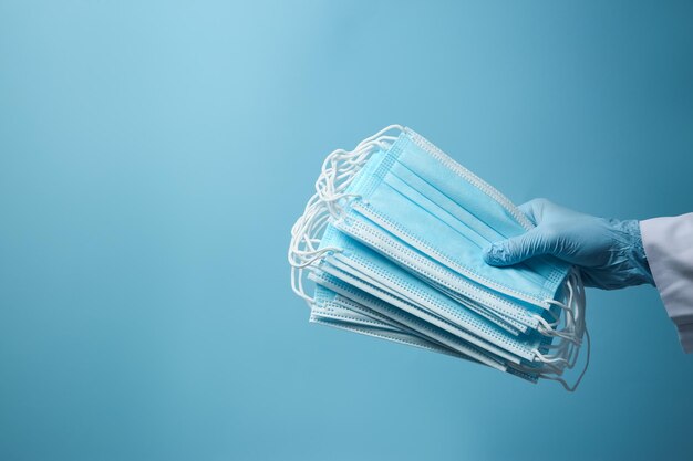 Doctor in latex gloves holding disposable face masks on light blue background closeup with space for text Protective measures during coronavirus quarantine