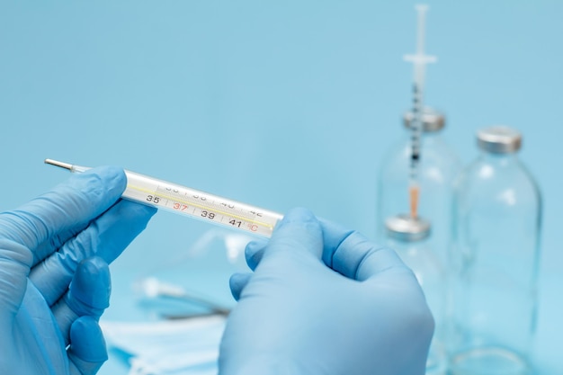 Doctor in latex gloves holding a glass mercury thermometer on blue background