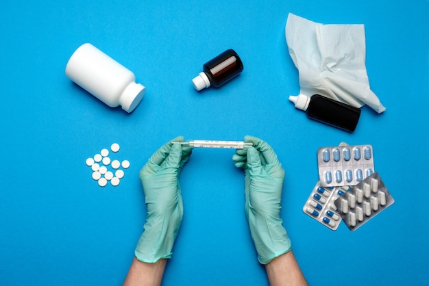 Doctor in latex gloves holding Mercury thermometer with pills