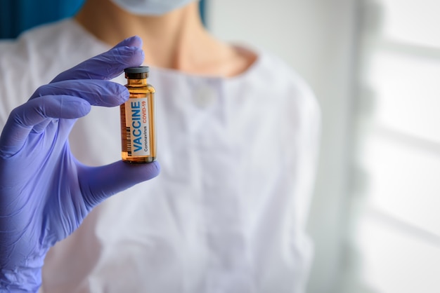 Doctor in latex gloves holding vial with COVID-19 vaccine