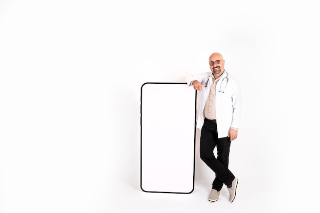 Doctor leaning life size smartphone with empty white screen for mock up. Isolated white background.