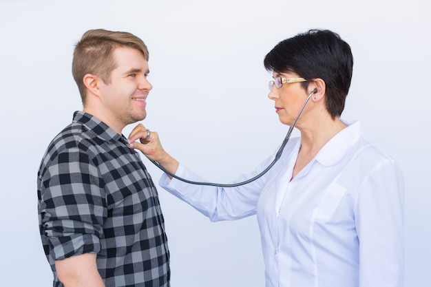 Doctor listening to cheerful young patient's chest with stethoscope over white background