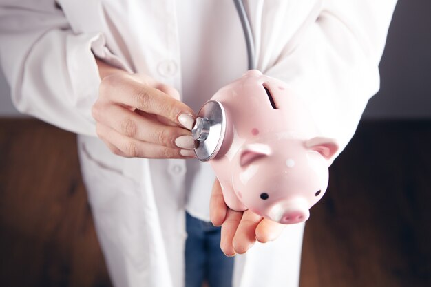 The doctor listens to the piggy bank with a stethoscope