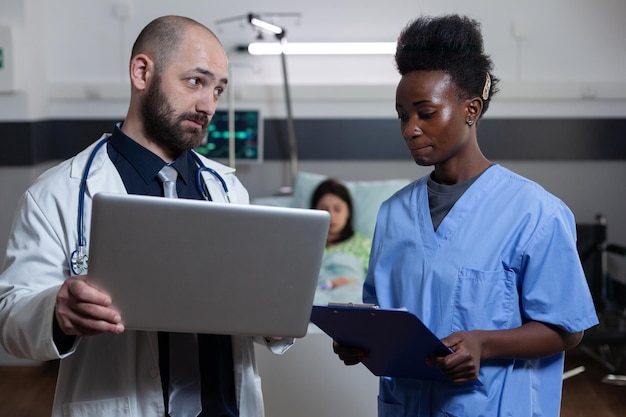 Medico che giudica l'infermiera dell'ospedale che si sente in colpa per aver ottenuto risultati di laboratorio sbagliati in piedi nel reparto dei pazienti. computer portatile della holding del medico che mostra la diagnostica all'operatore sanitario.