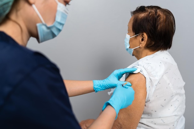 医師は、医療用マスクの高齢患者にCovid19またはコロナウイルスワクチンを注射します