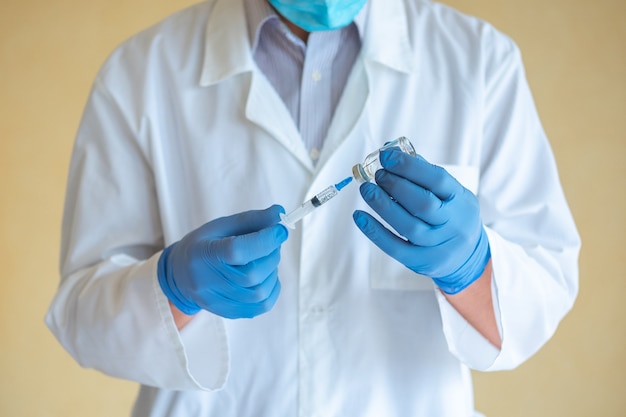 Doctor man in blue latex gloves dials a vaccine into a syringe