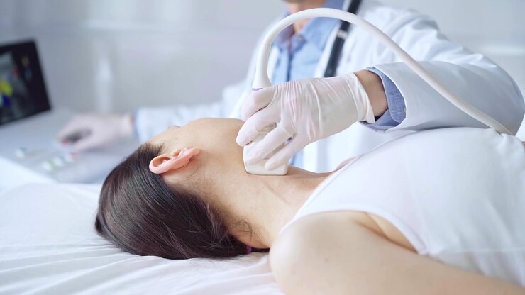 Photo 医師は,医学的検査のために横たわっている女性患者の首に超音波装置を使用しています. 医学と科学