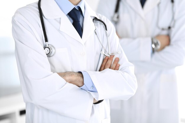 Doctor man standing straight and crossed arms with colleague at background, close-up. Group of doctors. Perfect medical service in clinic. Medicine and healthcare concepts. Toned picture.