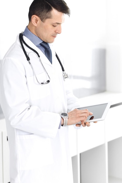 Doctor man using tablet computer for network research or virtual disease treatment. Perfect medical service in clinic. Happy future for modern medicine, medic data and healthcare concepts