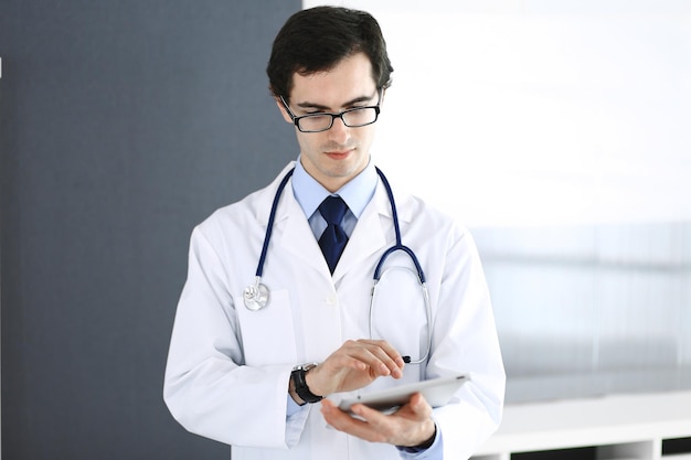 Doctor man using tablet computer for network research or virtual disease treatment. Perfect medical service in clinic. Modern medicine, medic data and healthcare concepts.