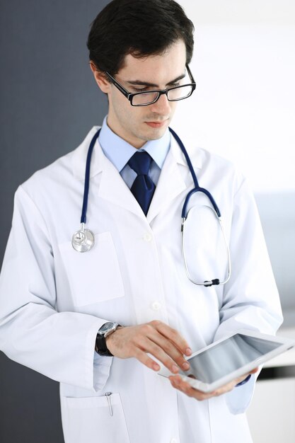 Doctor man using tablet computer for network research or virtual disease treatment. Perfect medical service in clinic. Modern medicine, medic data and healthcare concepts.